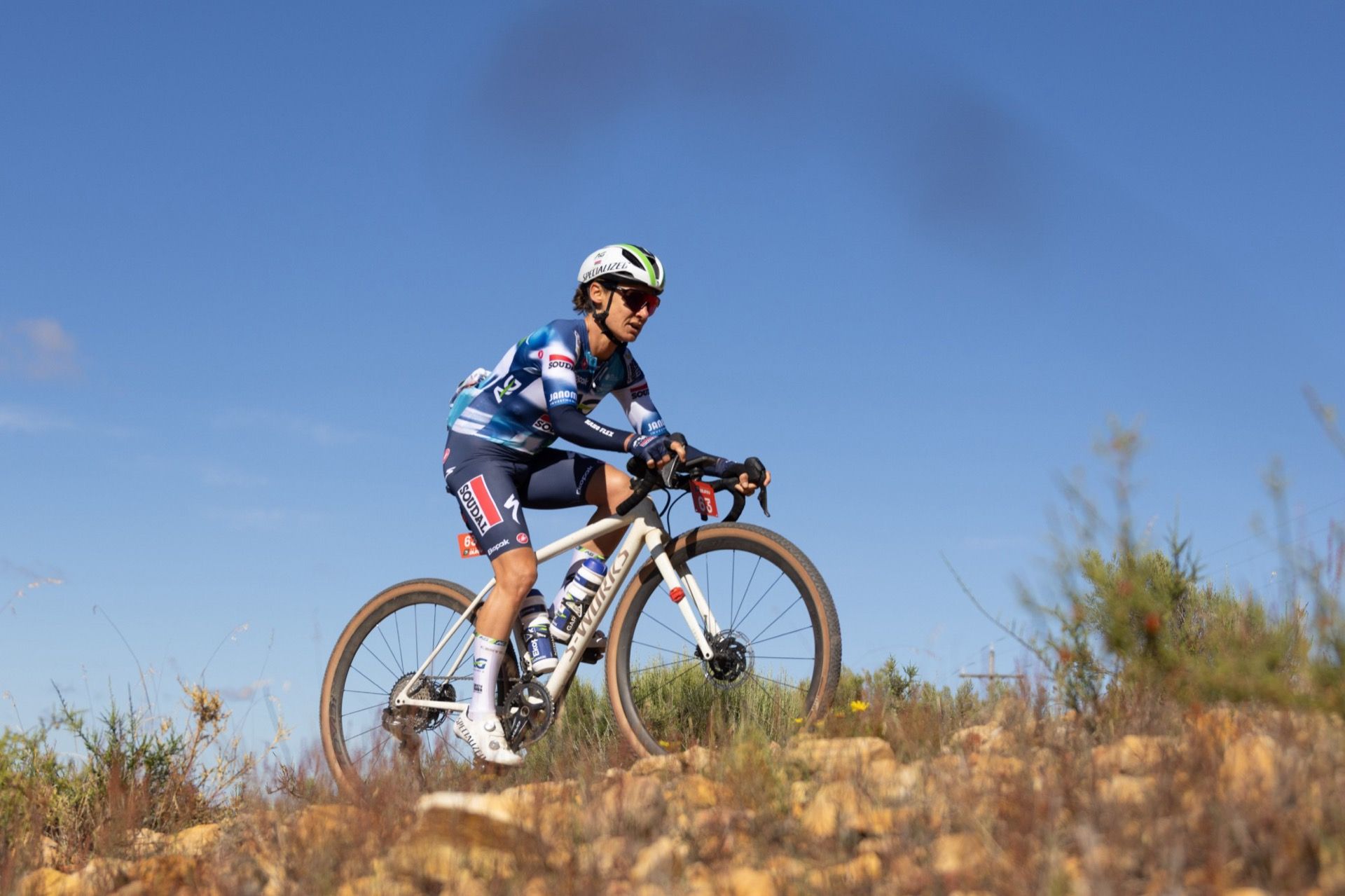 Ashleigh Moolman-Pasio climbing a rocky Karoo track on her gravel bike under a blue sky