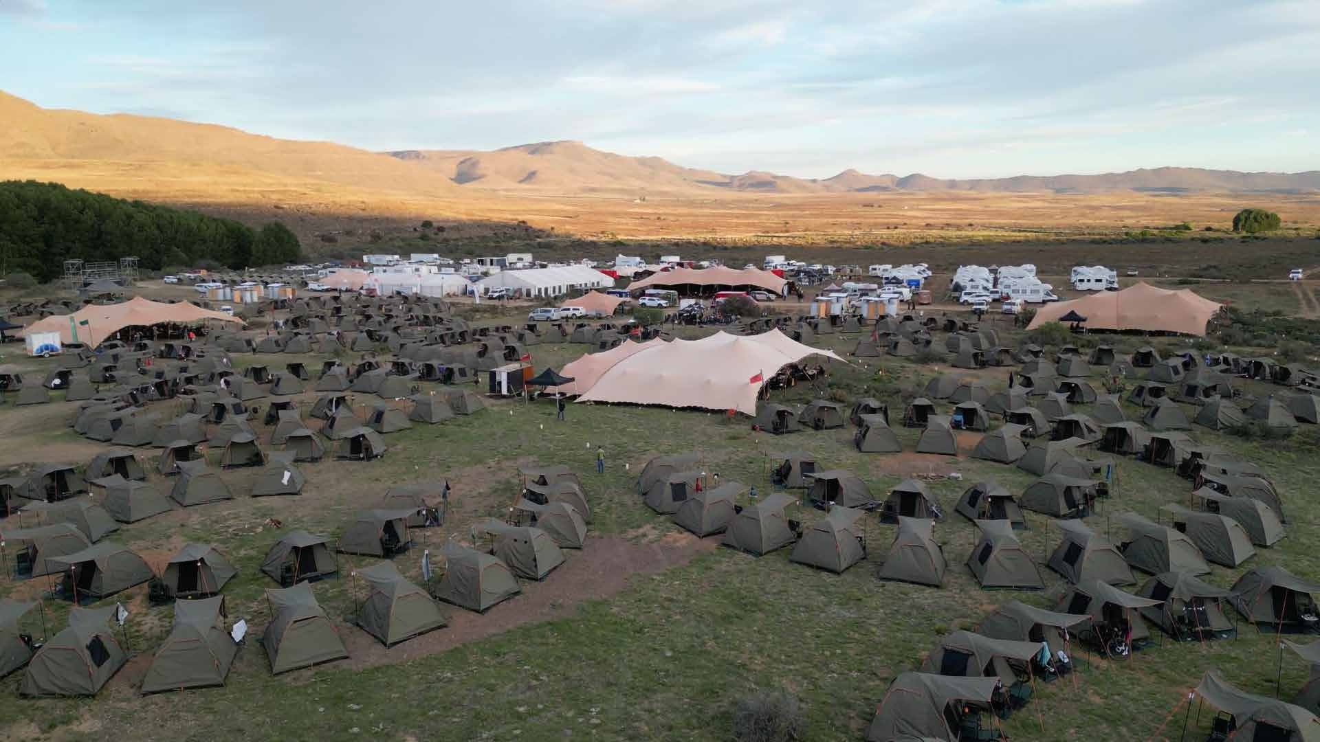 Aerial view of a Burn Camp at Blaauwater: rings of rider tents around a fire, stretch-tent lounges, and service tents beyond.