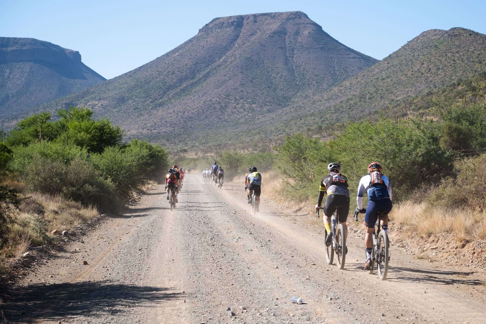 Riders on a dusty gravel road heading towards flat-topped Karoo mountains