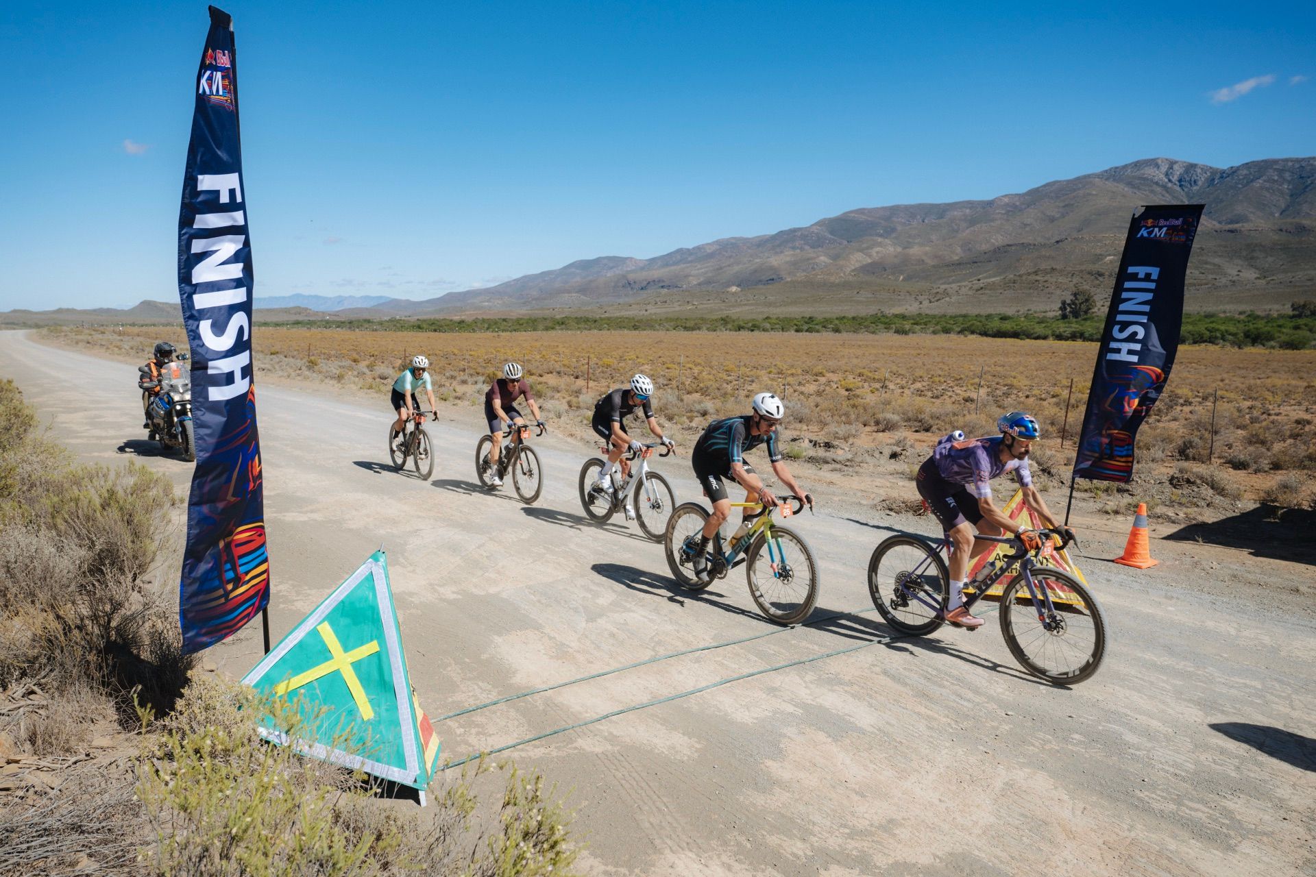 Riders sprinting through the Red Bull KM start and finish flags on a gravel road