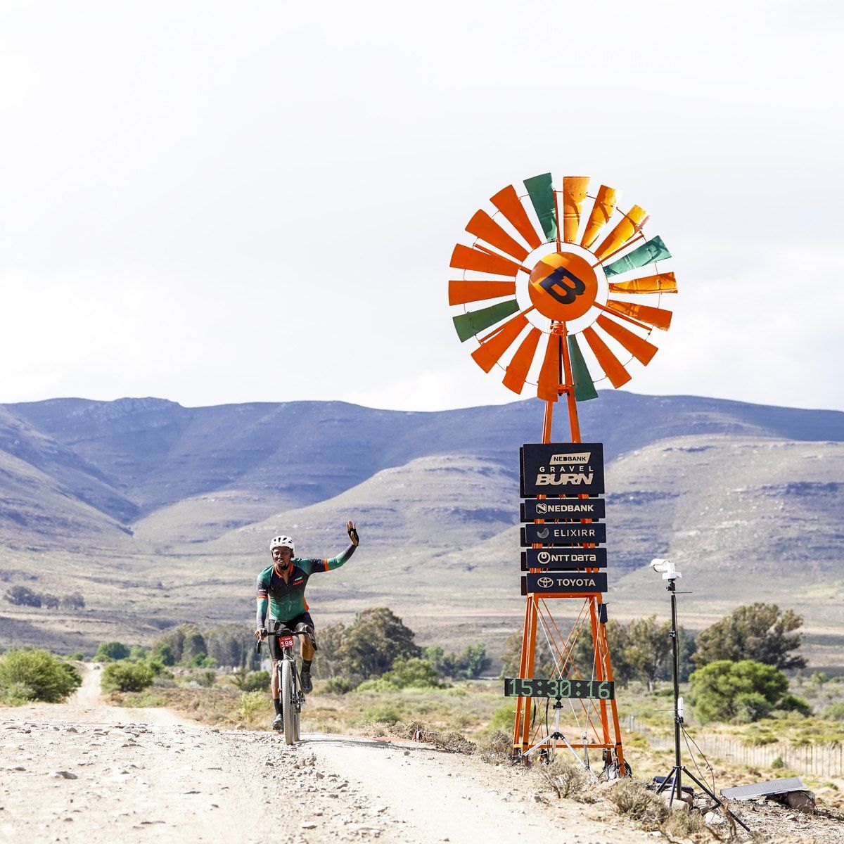 A rider raises an arm at the stage finish beside the Nedbank Gravel Burn windmill