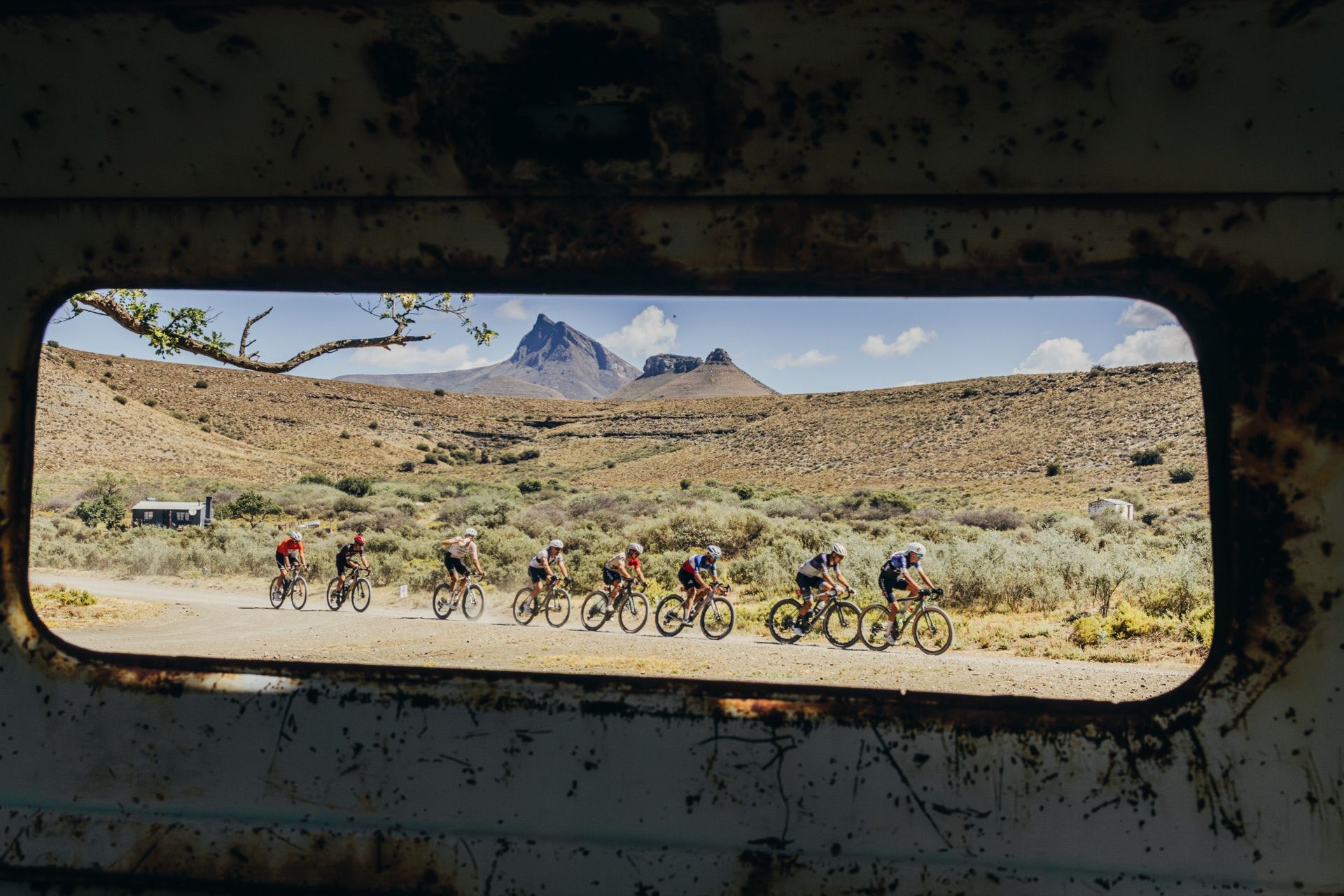 A group of riders seen through the window of an old farm vehicle, with Compassberg behind